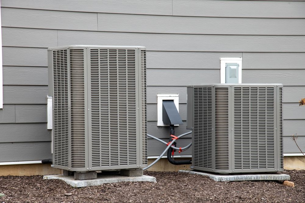 Two air conditioners are sitting on the side of a house.