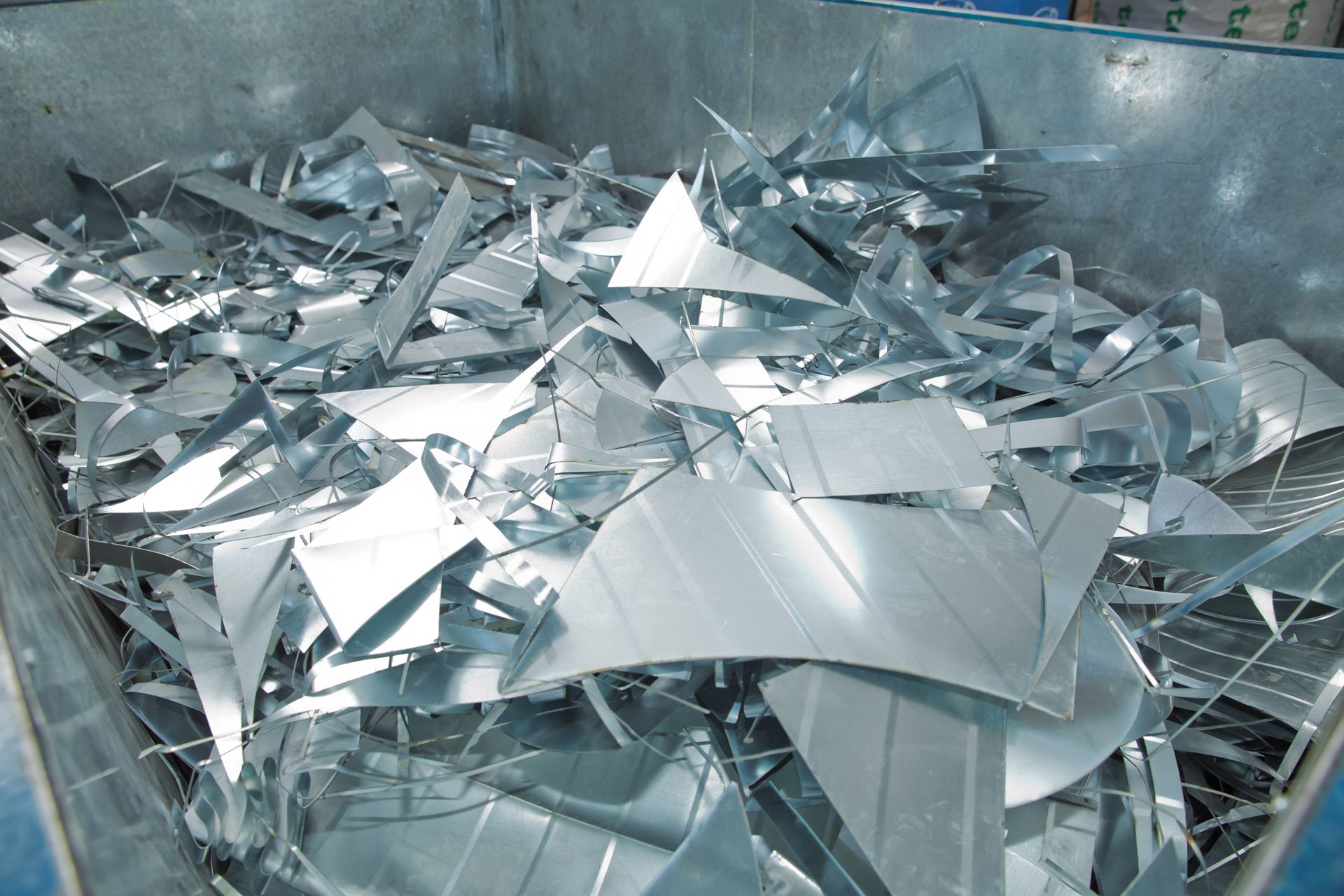 Scrap aluminum sheet offcuts piled inside a steel container at a metal recycling company facility.
