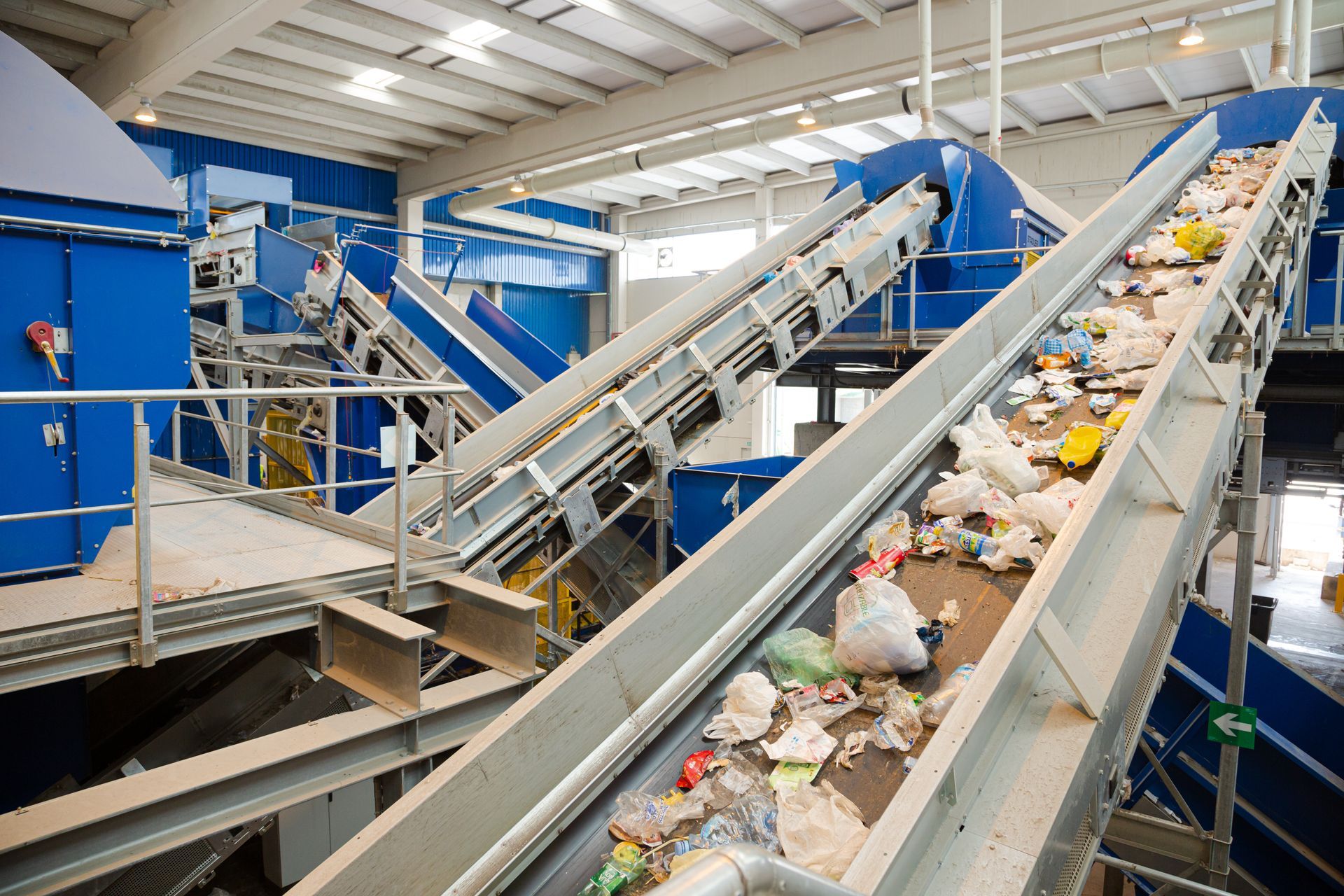 Conveyor belts carrying sorted plastics and packaging waste inside an industrial recycling center. Conveyor belts carrying sorted plastics and packaging waste inside an industrial recycling center.