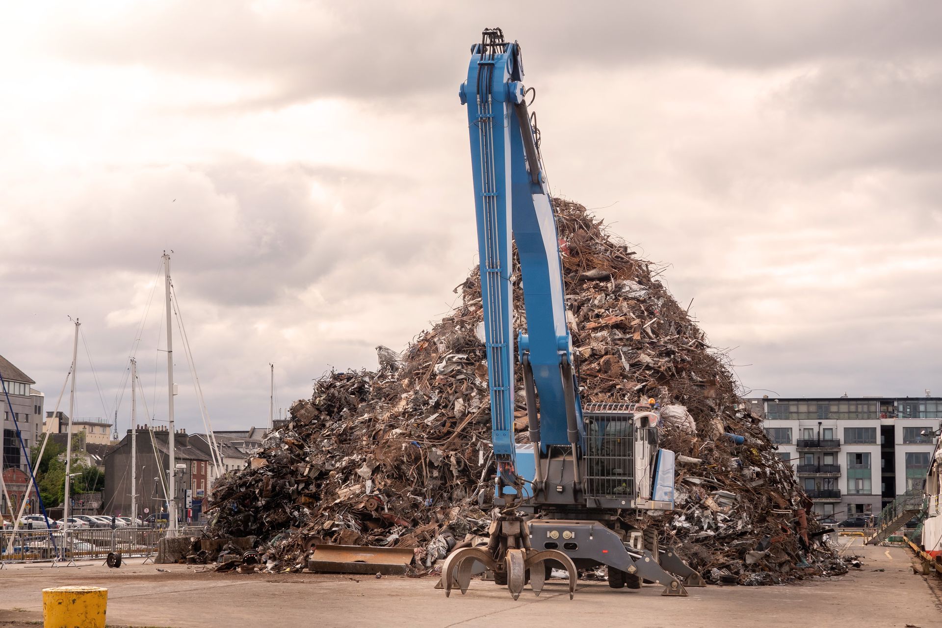 A blue industrial grapple crane in front of a large pile of scrap metal at an outdoor recycling yard A blue industrial grapple crane in front of a large pile of scrap metal at an outdoor recycling yard