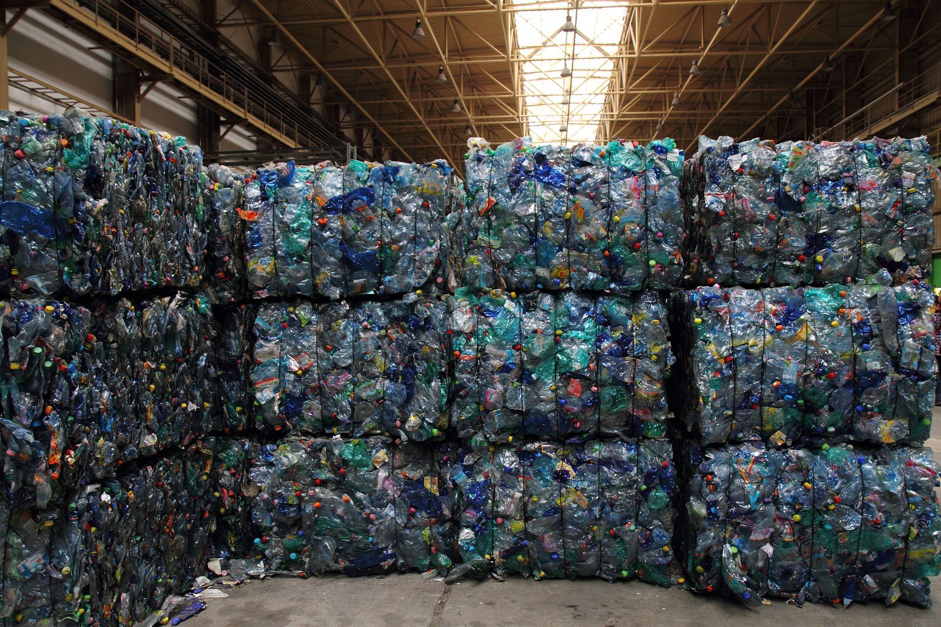 Tightly baled plastic bottles stacked in rows inside a bright warehouse at a busy recycling center. Tightly baled plastic bottles stacked in rows inside a bright warehouse at a busy recycling center.