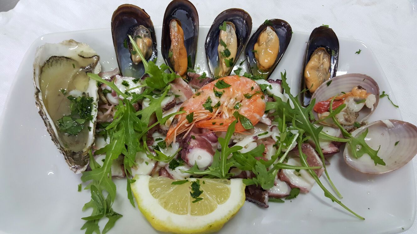 Piatto di frutti di mare con salmone, cozze, vongole, fetta di limone e verdure su un piatto bianco.