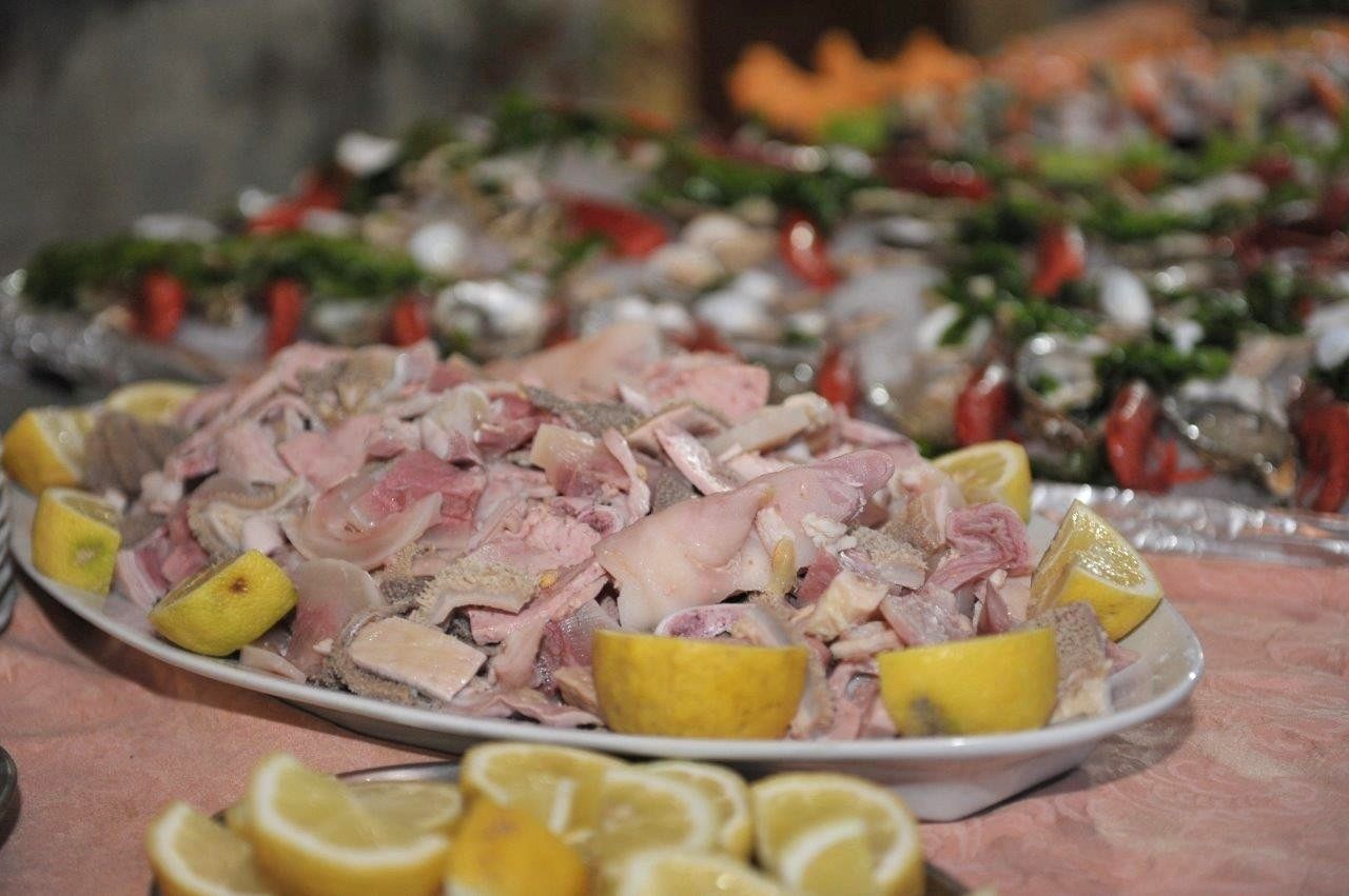 Piatto di pesce tritato con spicchi di limone su un tavolo da buffet, con insalata sullo sfondo.
