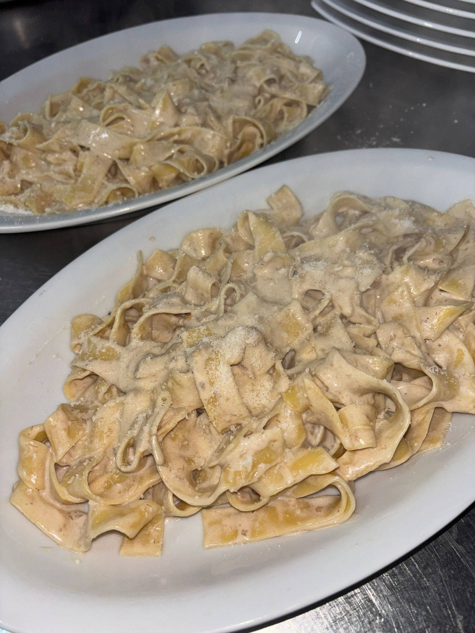 Due piatti di pasta cremosa su vassoi ovali bianchi in un ambiente da cucina.