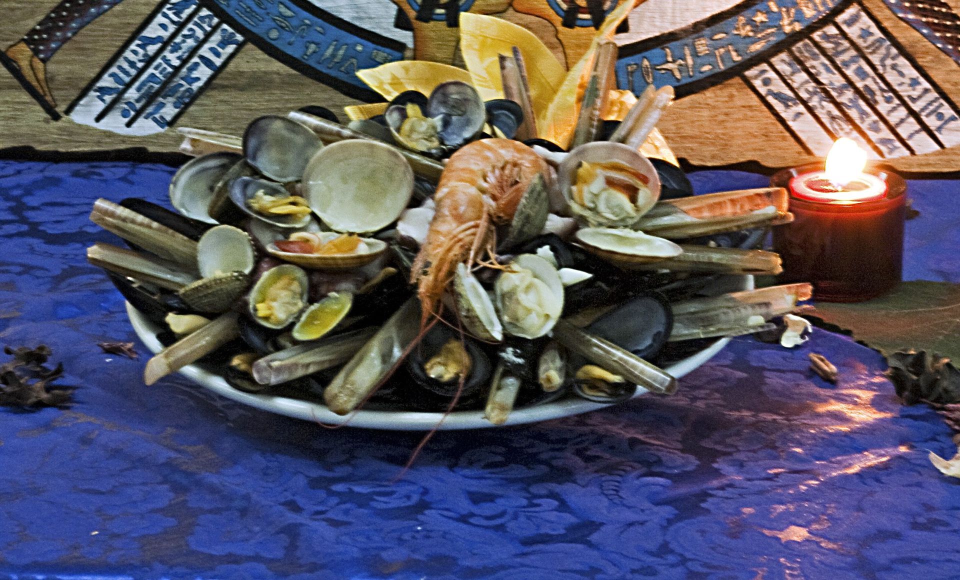 Un tavolo blu con un mucchio decorativo di conchiglie e una candela accesa nelle vicinanze.
