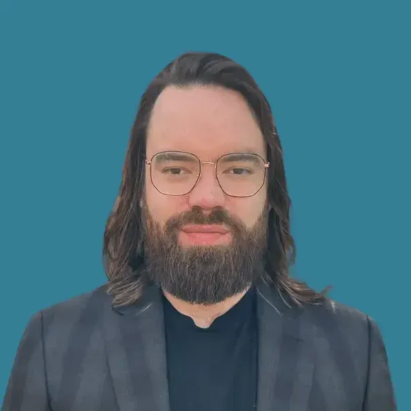 A man with a beard and glasses is wearing a suit and a black shirt.