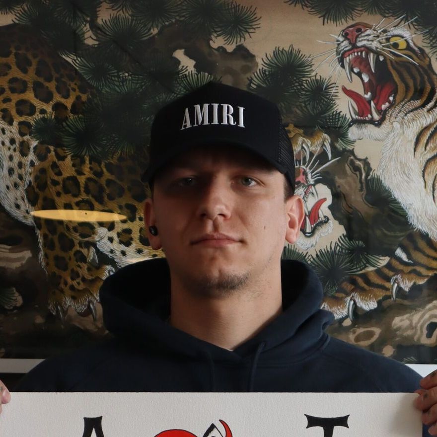 A man wearing a amiri hat holds a sign in front of a painting of a tiger
