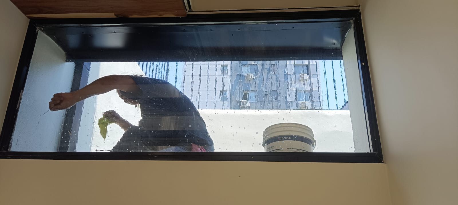 Una persona extiende la mano a través de una ventana abierta hacia el exterior de un edificio.