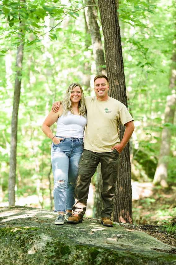 A man and a woman are standing next to each other on a rock in the woods.