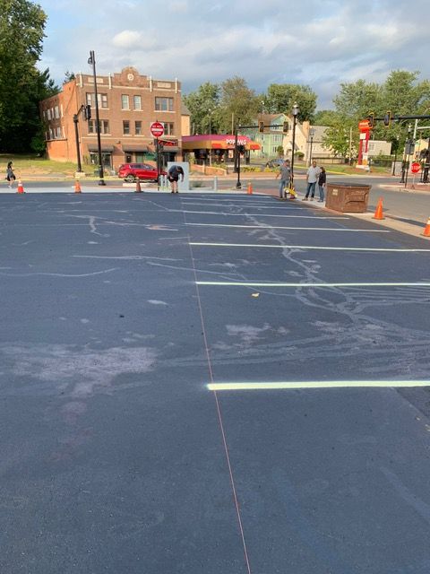 Parking lot with new blue asphalt and white lines. Workers in background. Buildings and street in background.