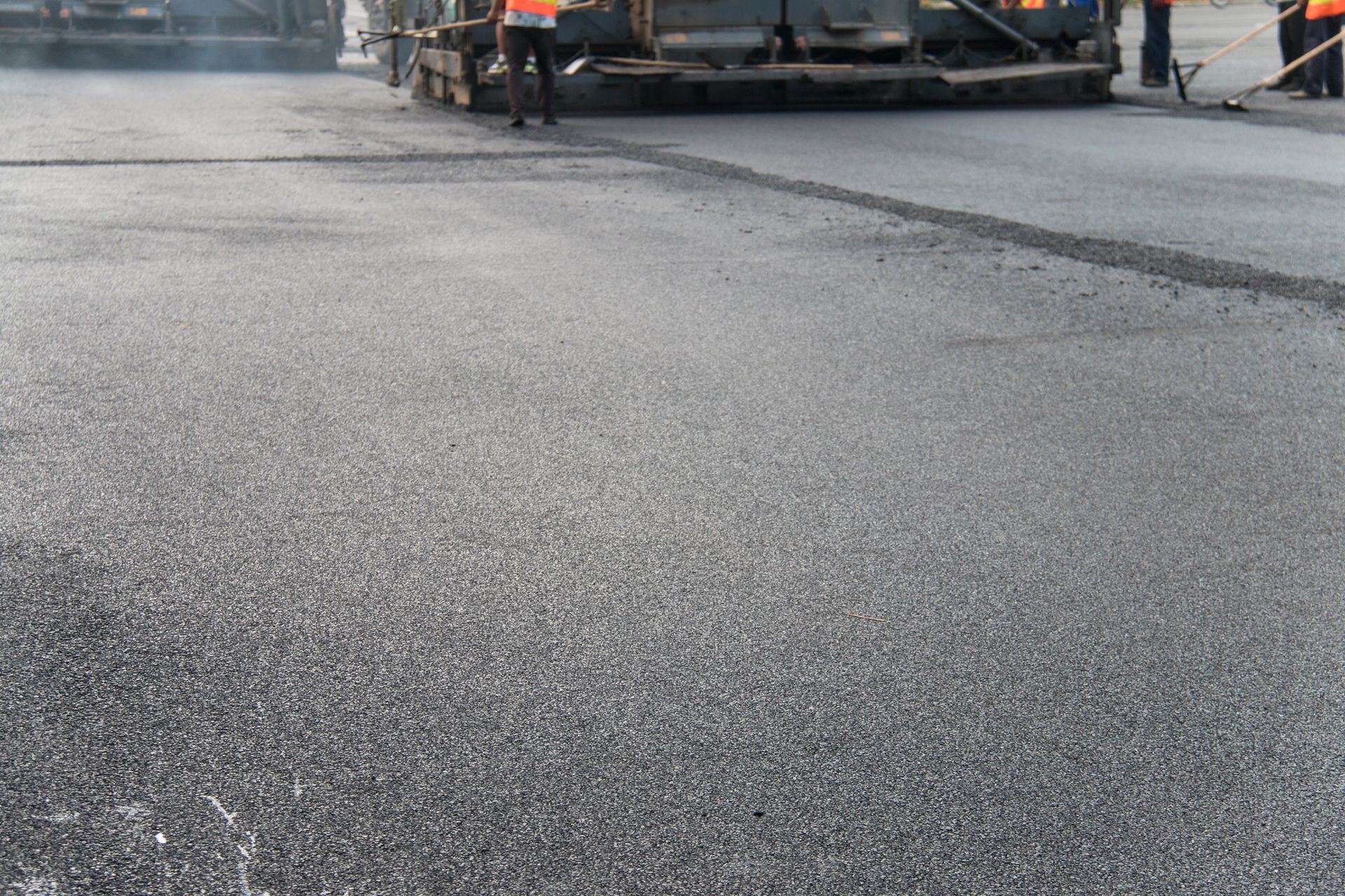 Construction crew paving fresh hot asphalt road with industrial paving machine.