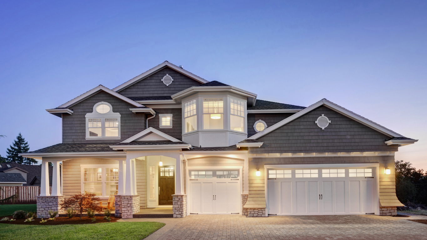 Well-lit suburban two-story house with gray siding and attached garage at dusk