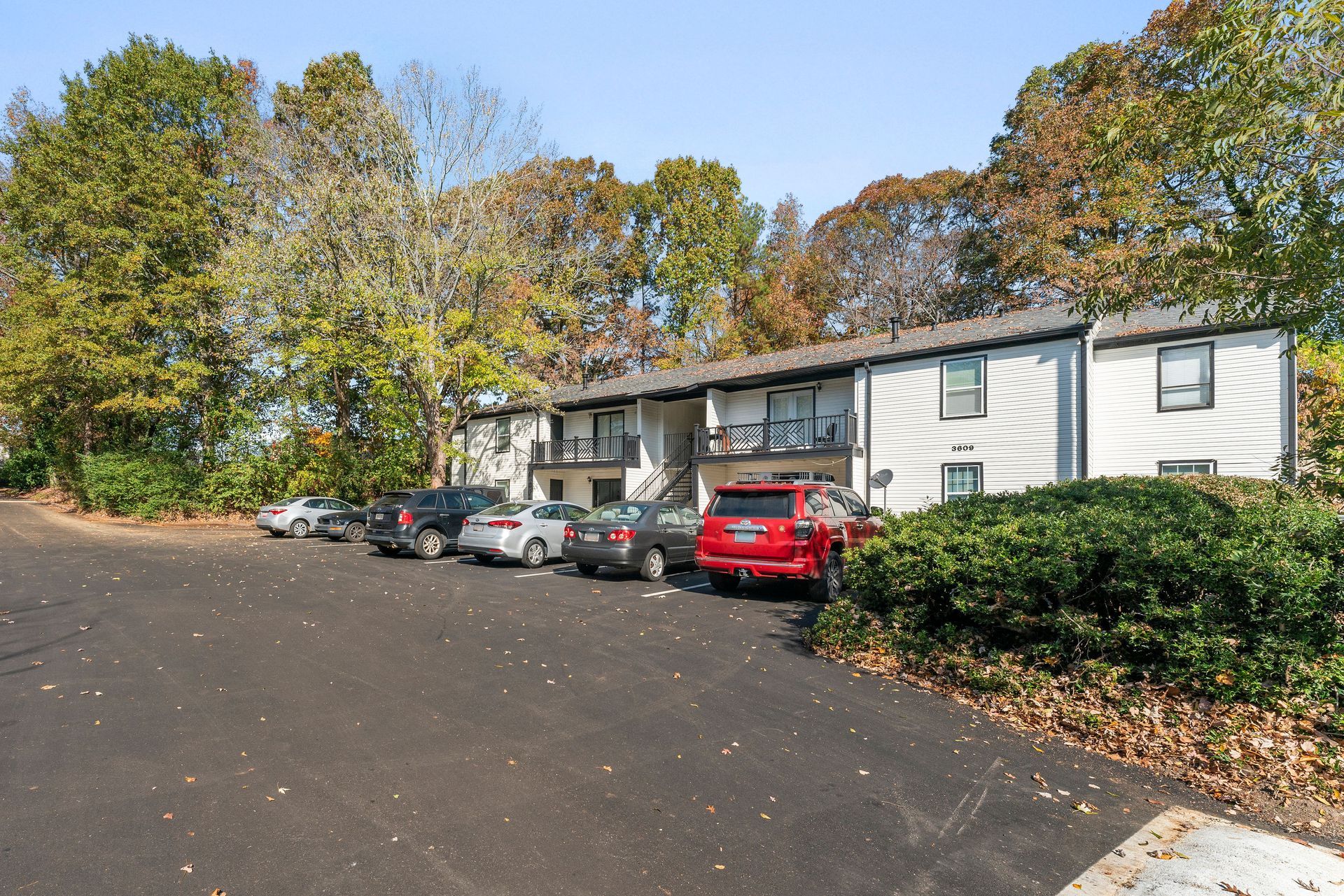 Apartment complex with parked cars beside a tree-lined lot on a sunny day
