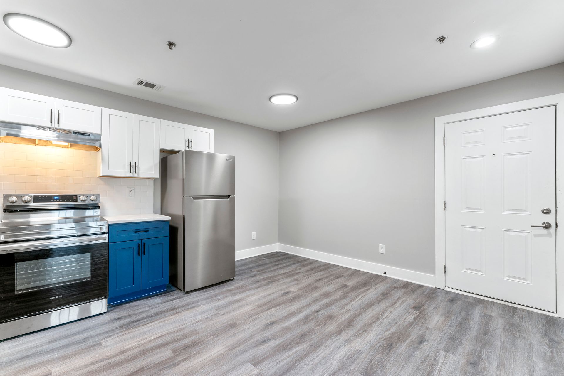 Empty modern kitchen with stainless steel appliances, white cabinets, gray flooring, and a door on the right