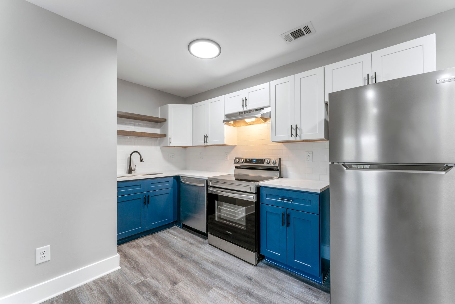 Modern kitchen with blue cabinets, white uppers, stainless fridge, and gas stove