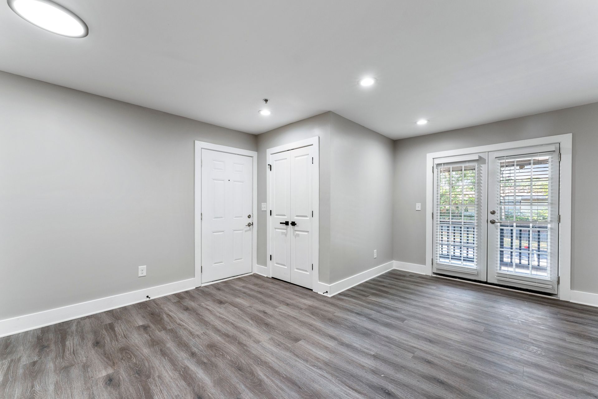 Empty gray room with wood floors, recessed lights, double closet doors, and glass doors to a balcony.