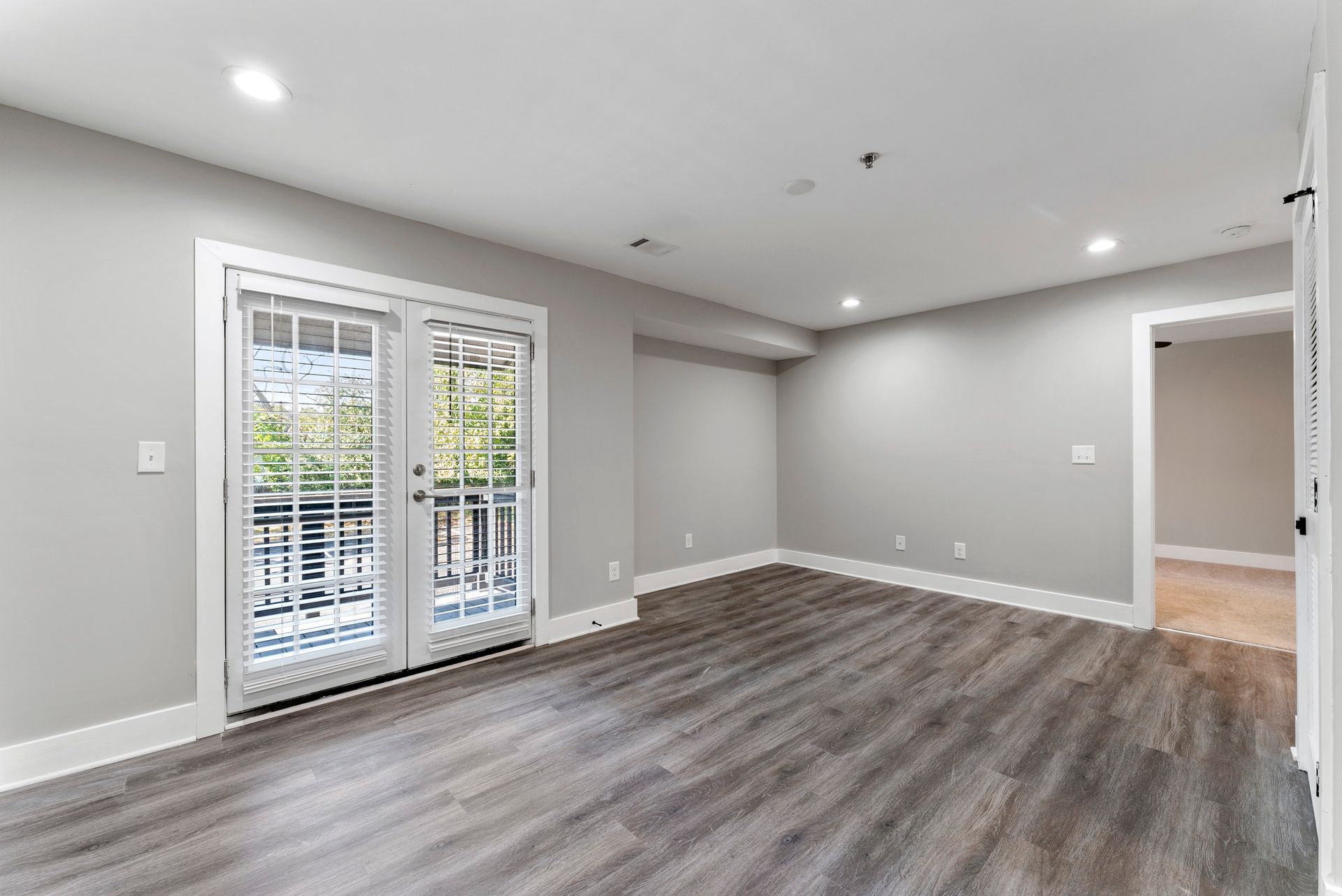 Empty modern living room with gray walls, wood-look floors, and sliding glass doors to a patio