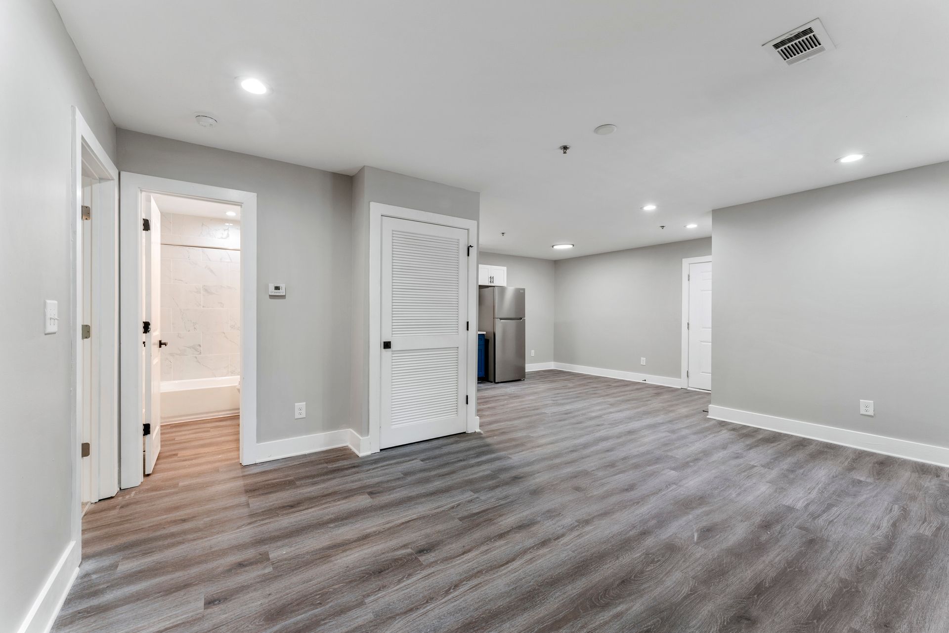 Empty modern living room with gray walls, wood-look floors, and recessed ceiling lights
