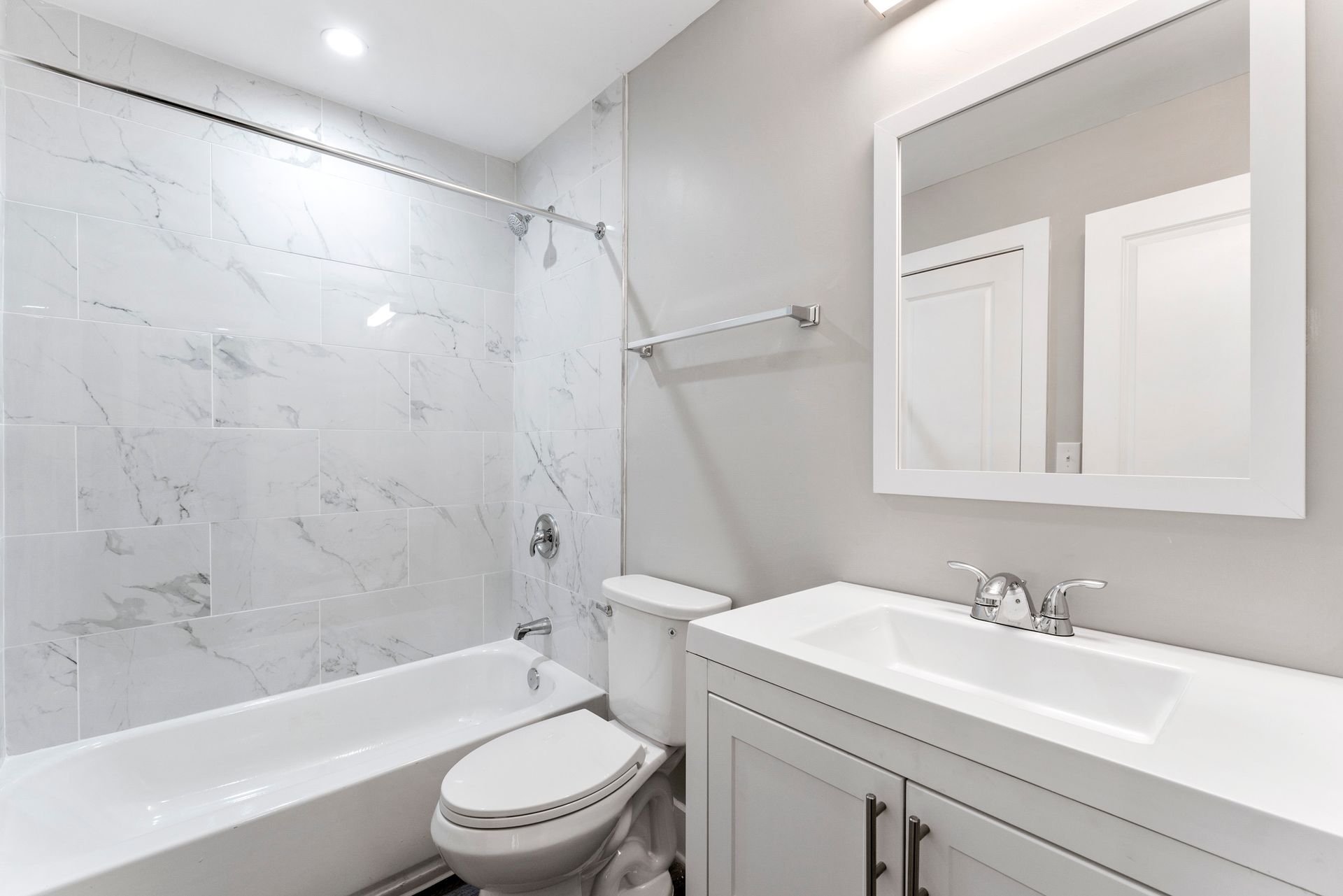 Bright white bathroom with bathtub, toilet, vanity sink, and large mirror.