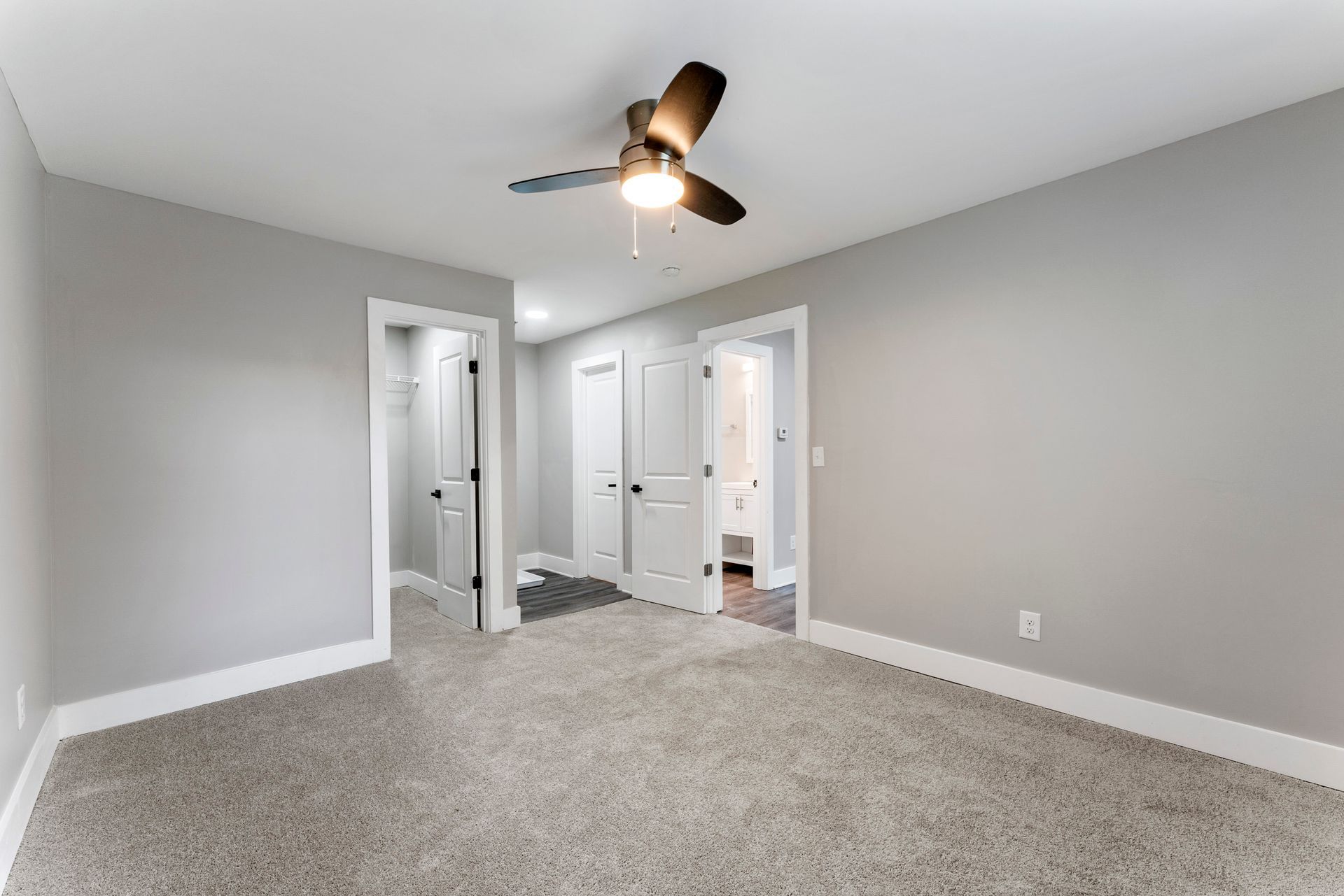 Empty gray bedroom with carpet, ceiling fan, and two open doorways to a bathroom or closet.