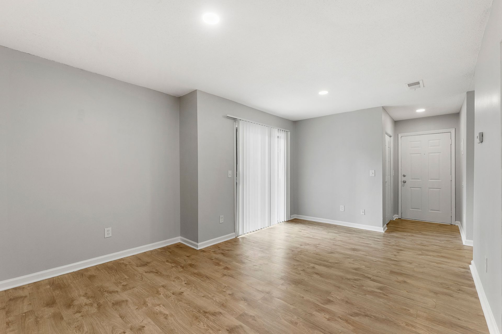 Empty gray living room with wood floors, recessed lights, and white doors.