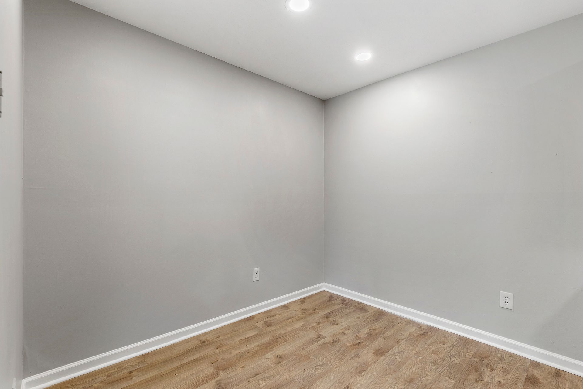 Empty gray room with white trim, recessed ceiling lights, and wood flooring