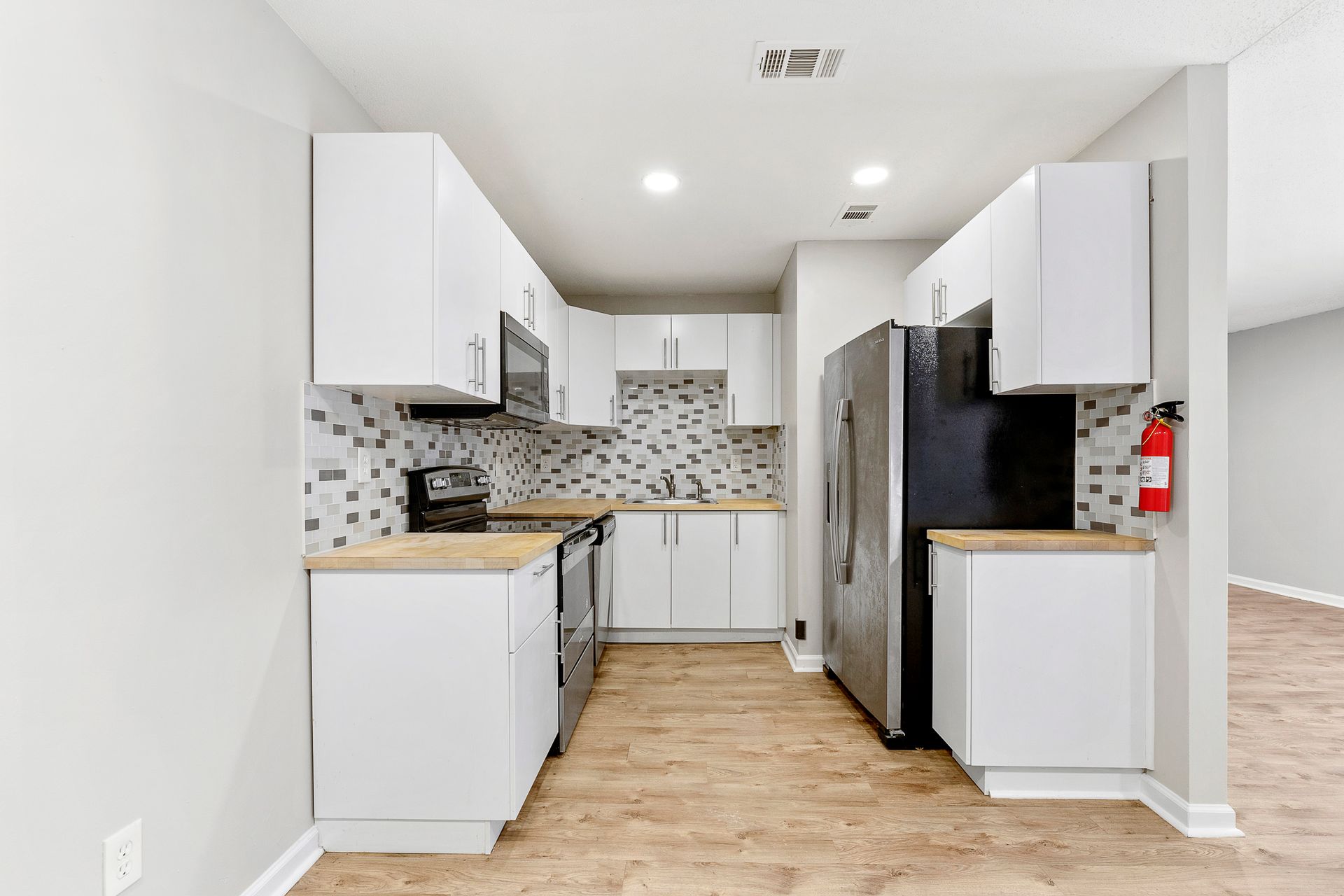 Bright modern galley kitchen with white cabinets, wood floor, and mosaic tile backsplash