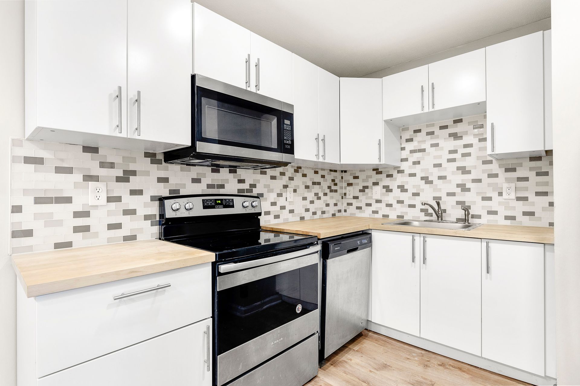 Bright white kitchen with stainless steel stove, microwave, dishwasher, and mosaic tile backsplash