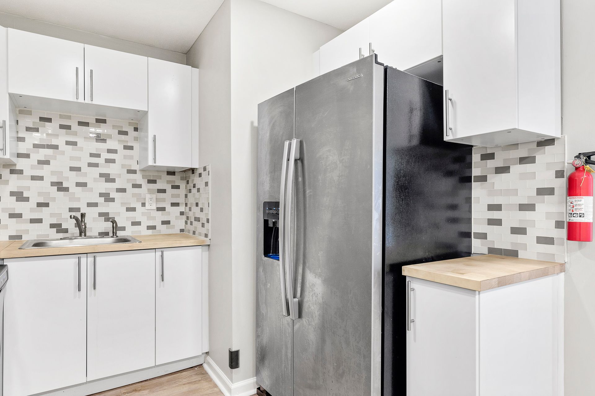 Modern kitchen with white cabinets, mosaic backsplash, and stainless steel refrigerator