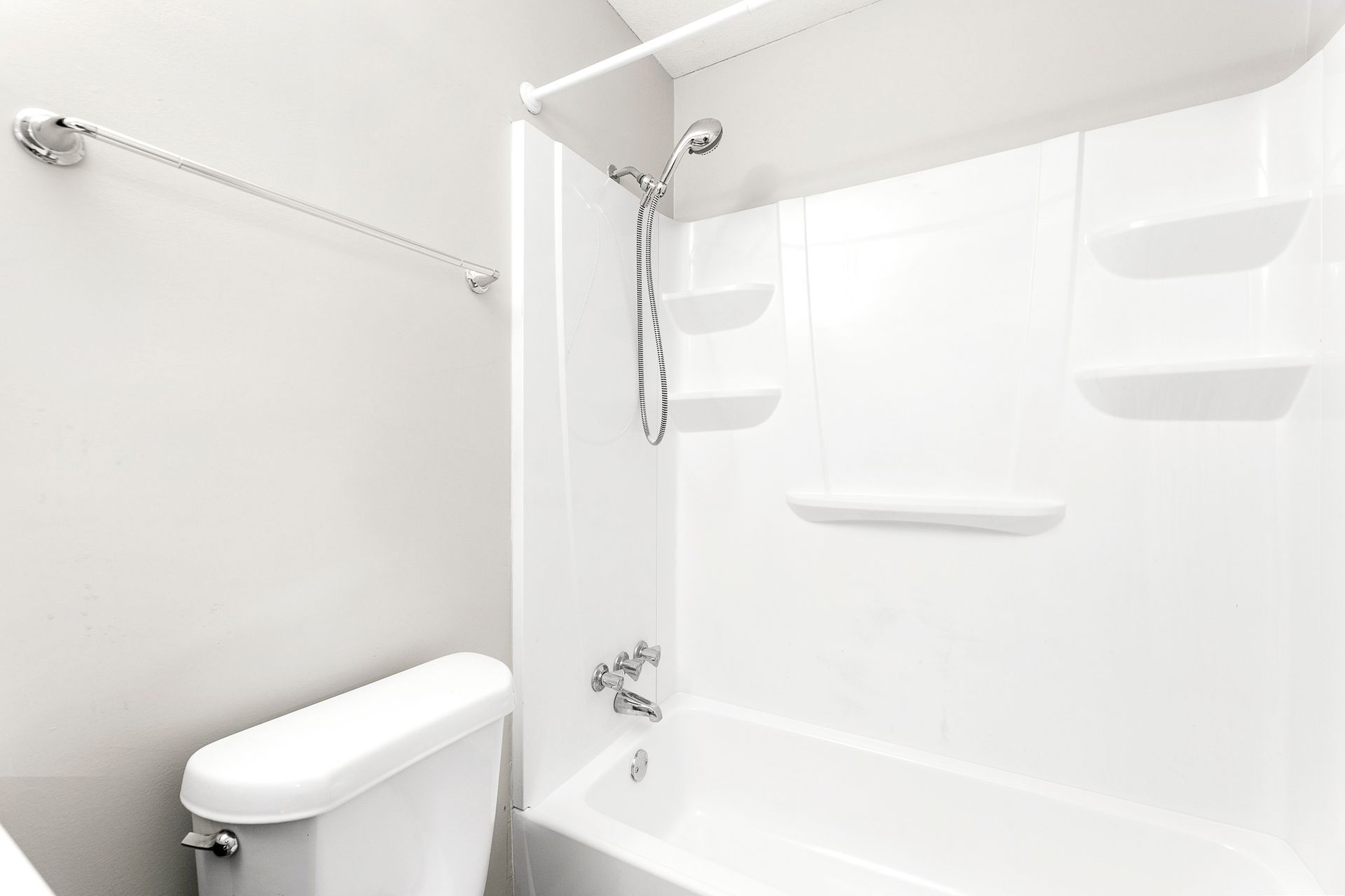 White bathroom with bathtub, shower curtain rod, towel bar, and toilet.