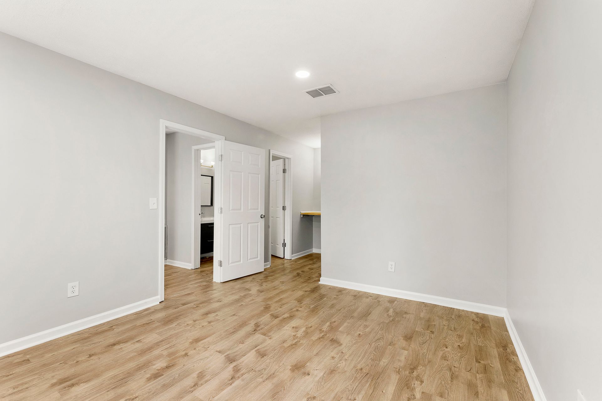 Empty white bedroom with light wood flooring and an open doorway to a hallway