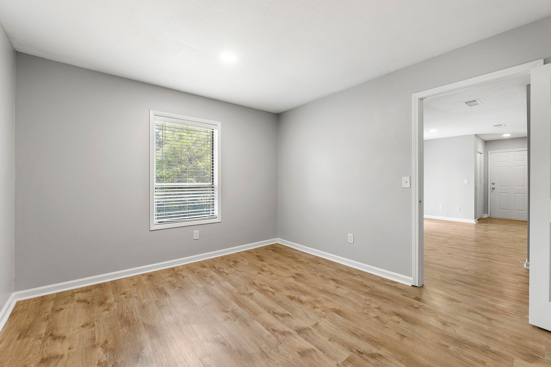 Empty gray bedroom with wood floors, a small window, and an open doorway to a closet area