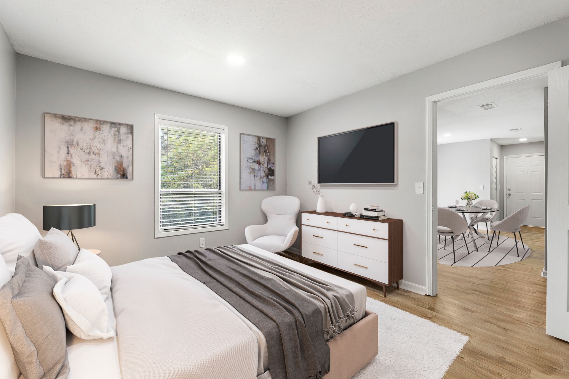 Bright modern bedroom with a bed, dresser, wall-mounted TV, and open doorway to a dining area