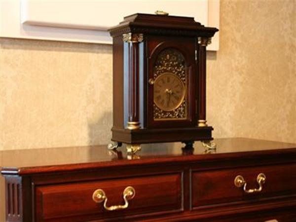 Ornate antique mantel clock on a polished wooden dresser against a beige wall