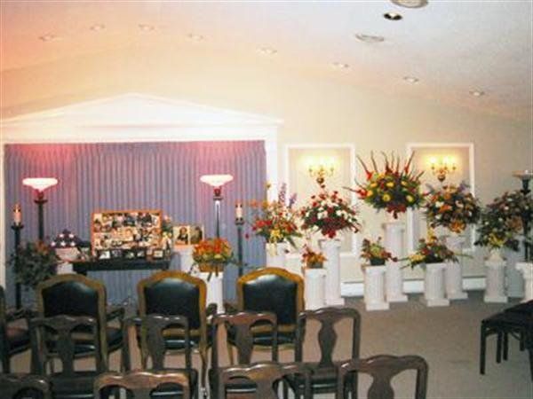 Flower-draped casket at the front of a funeral service room with rows of empty chairs