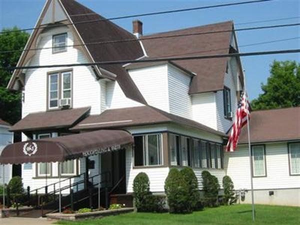 White house with brown roof, front porch, and American flag by a quiet street under clear skies