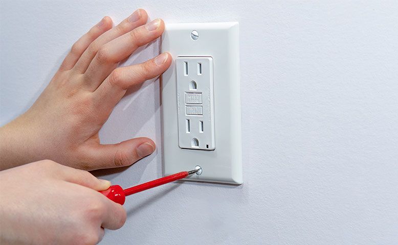 A person is installing an electrical outlet on a wall with a screwdriver.
