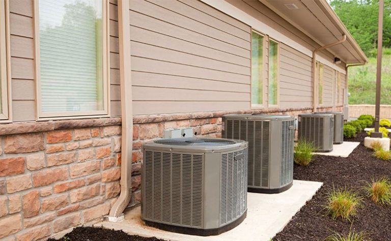 A row of air conditioners on the side of a house.
