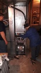 A man is working on an air conditioner in a basement.