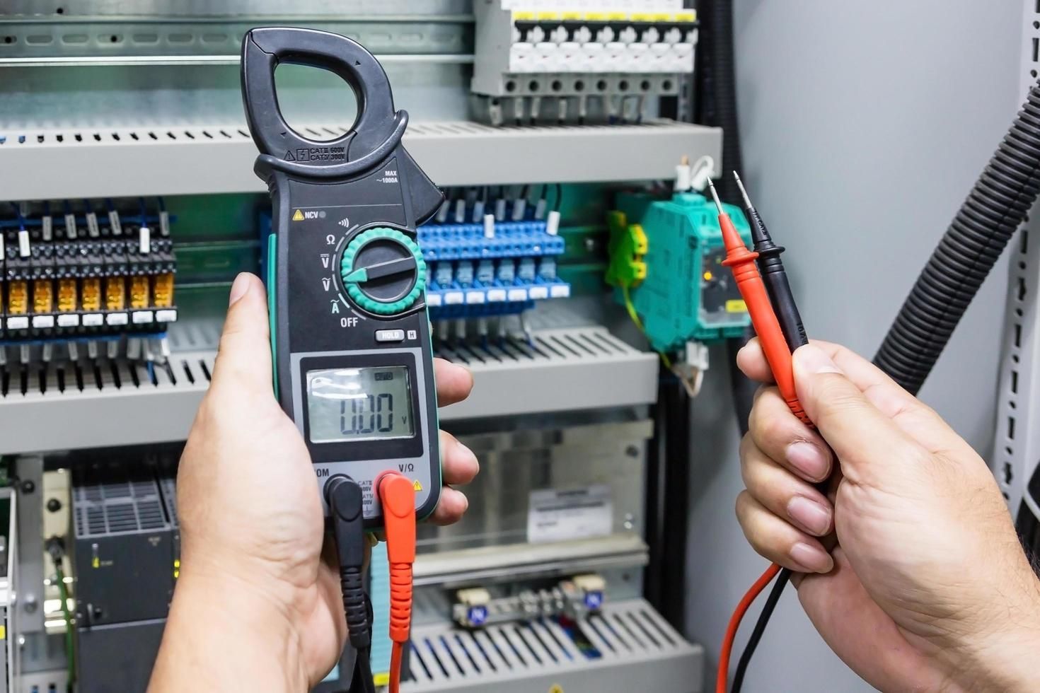 A person is holding a clamp meter and a multimeter in their hands.