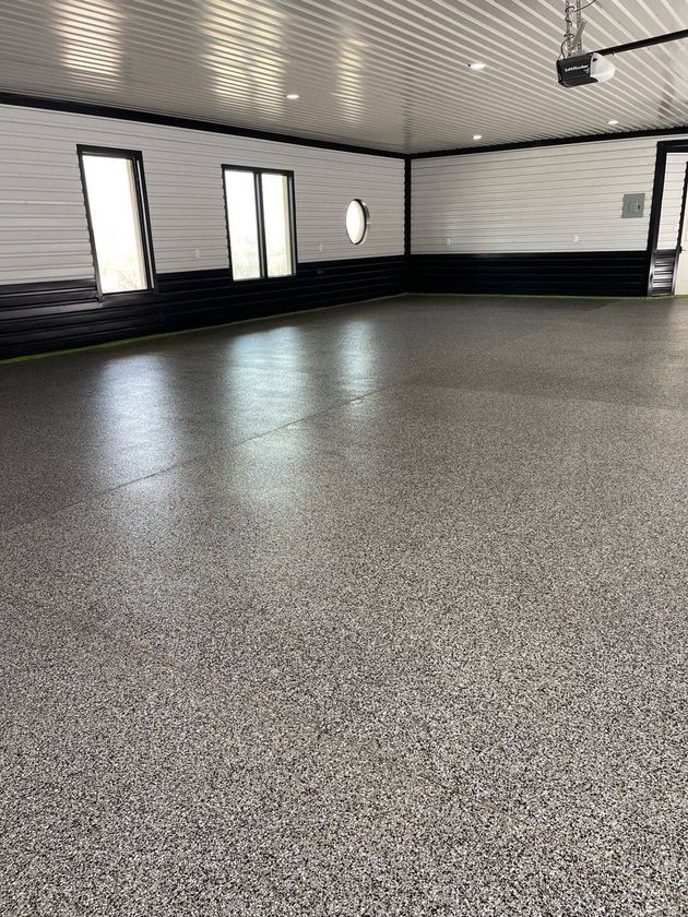 Empty indoor gym with speckled flooring, white walls, black trim, and ceiling lights