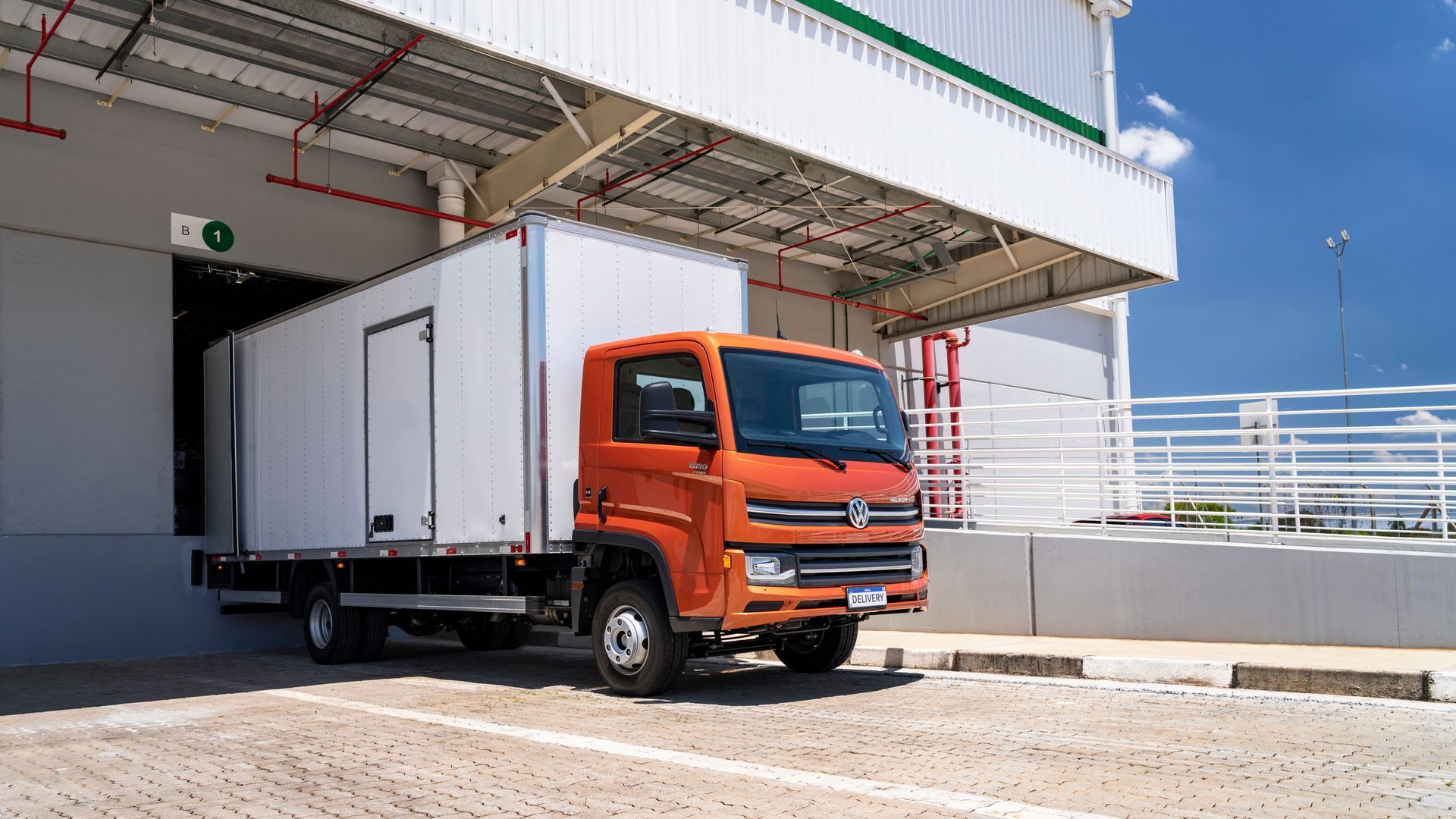 Un camión naranja está estacionado frente a un almacén.
