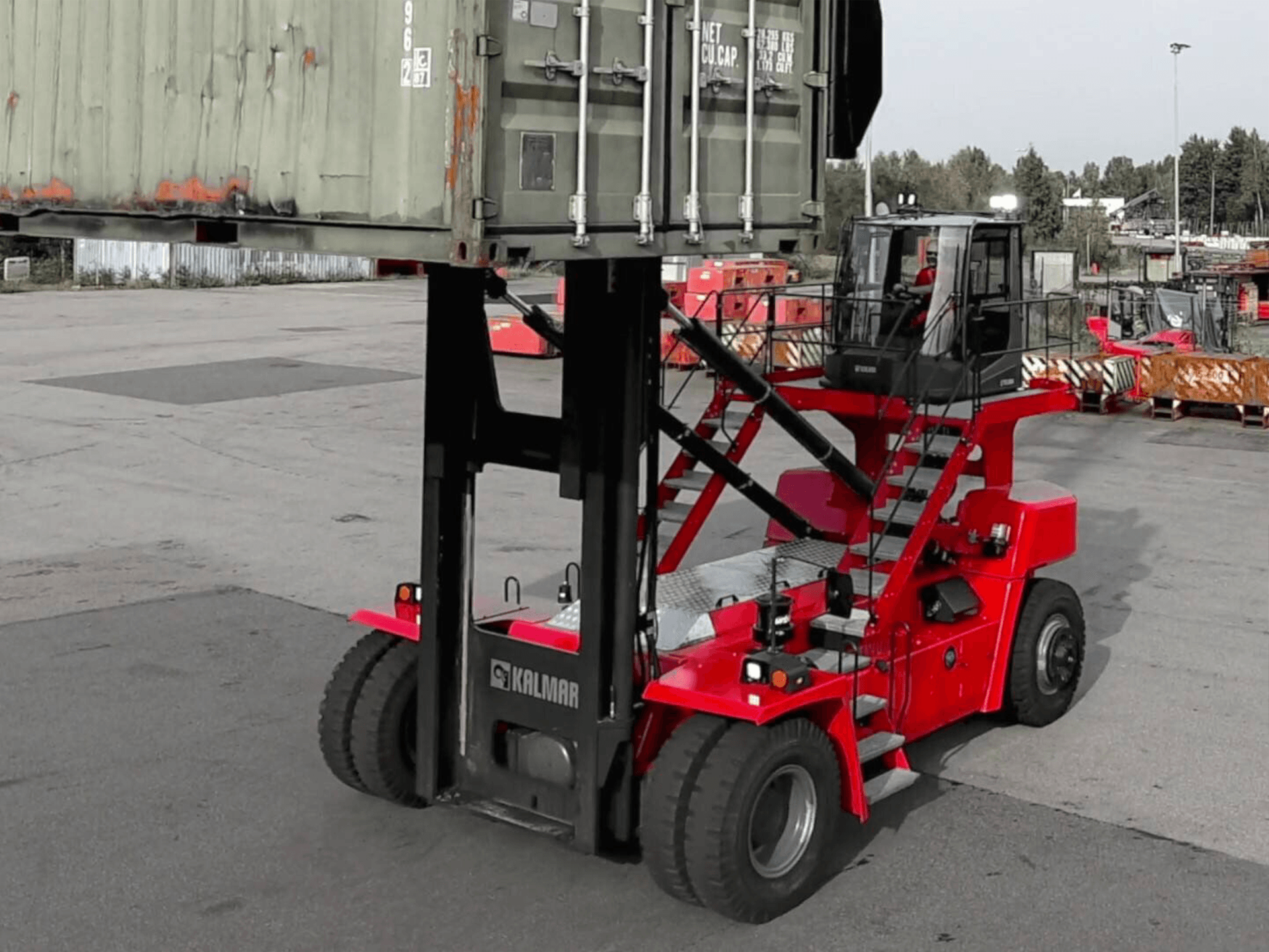 Una carretilla elevadora roja está levantando un contenedor de envío verde.