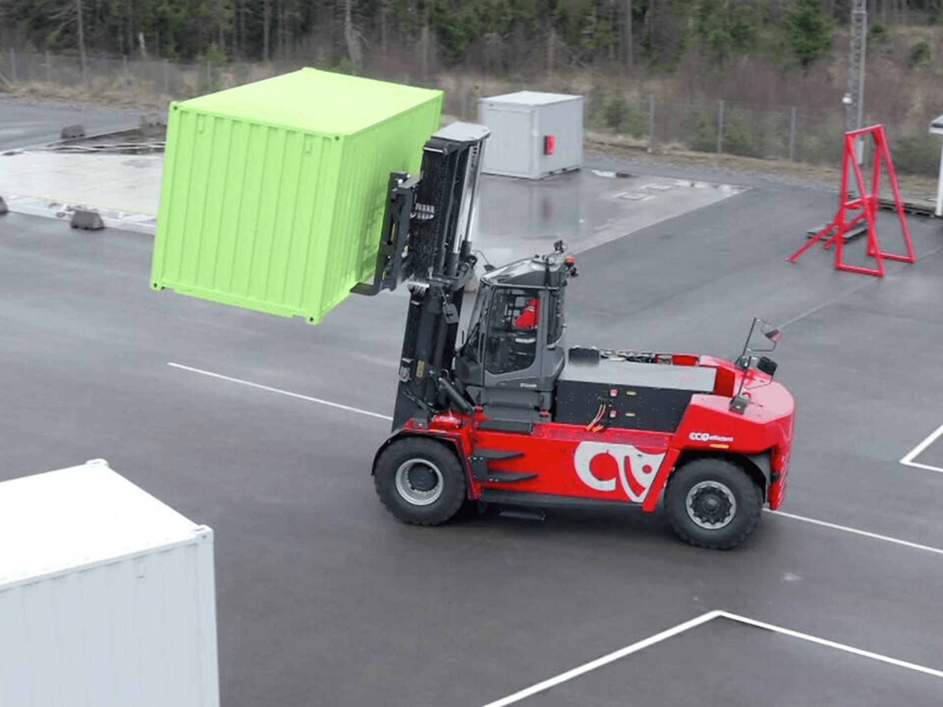 Una carretilla elevadora roja está levantando un contenedor verde en un estacionamiento.