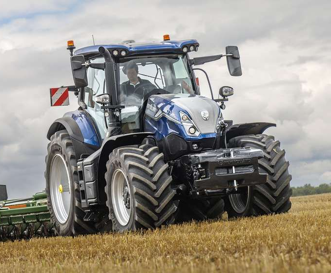 Un tractor azul circulando por un campo bajo un cielo nublado.