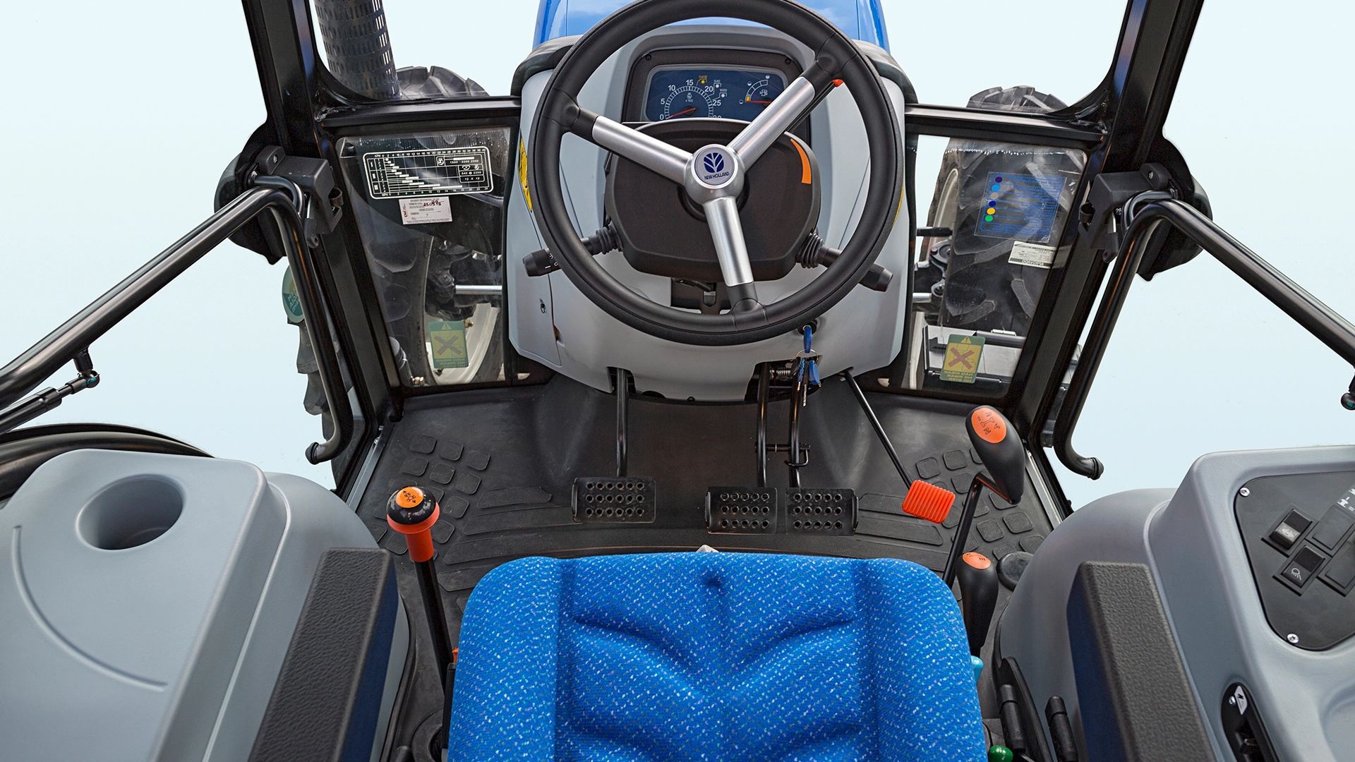 El interior de un tractor con asientos azules y un volante.