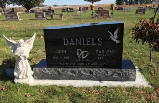 Black Daniels gravestone in a cemetery with white angel statue beside it.