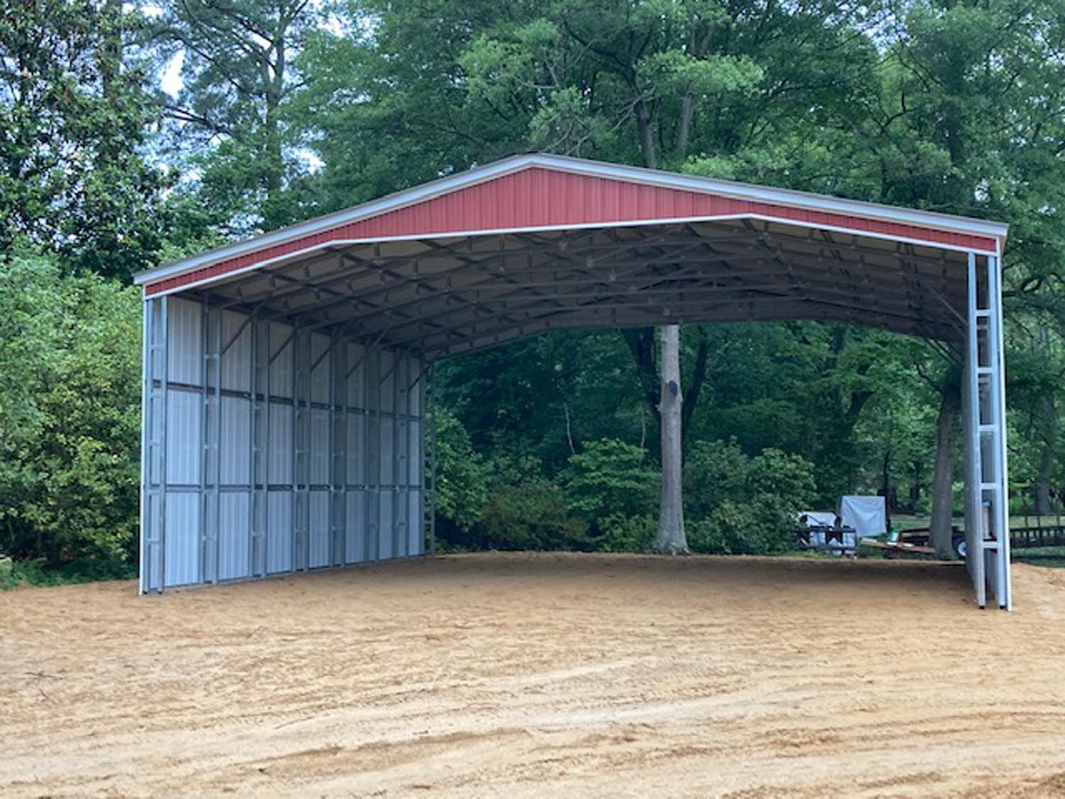 A large metal building with a red roof is sitting in the middle of a dirt field.
