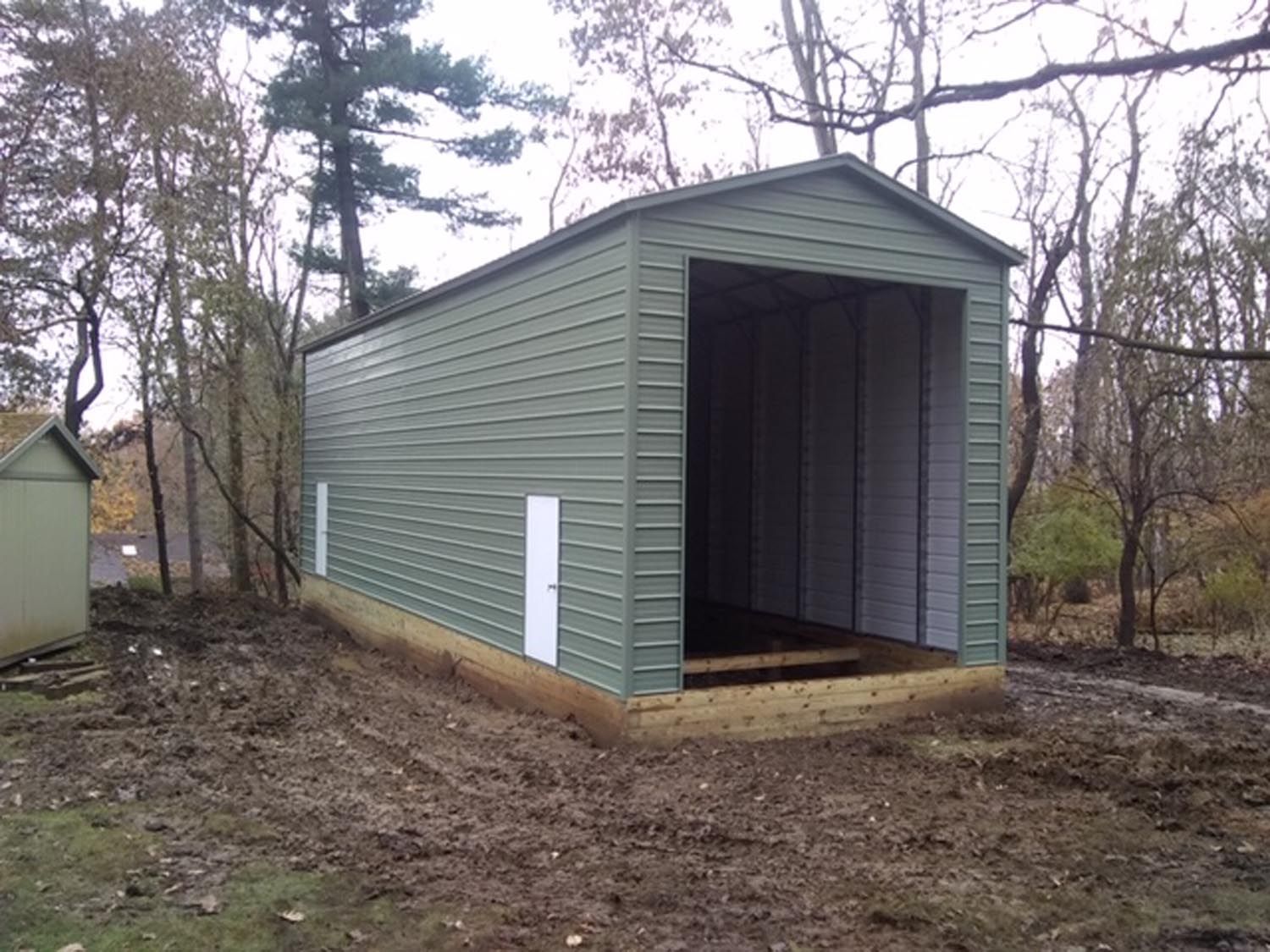 A green metal garage is sitting in the middle of a dirt field.