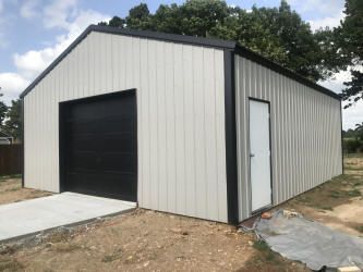 A metal garage with a black garage door and a white door.